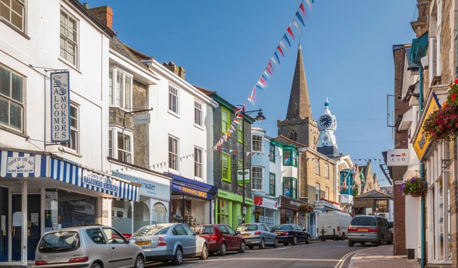 Colourful shops and church spire along a sunny Kingsbridge high street with bunting